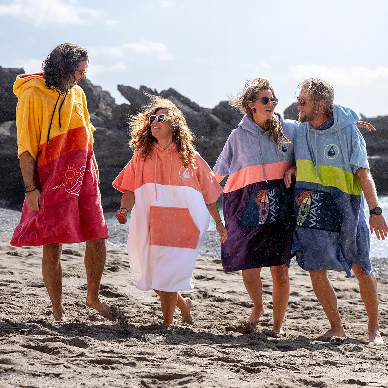 Vier Personen in gestreiften Badeponchos umarmen sich am Felsstrand, Ponchos von WAVE HAWAII